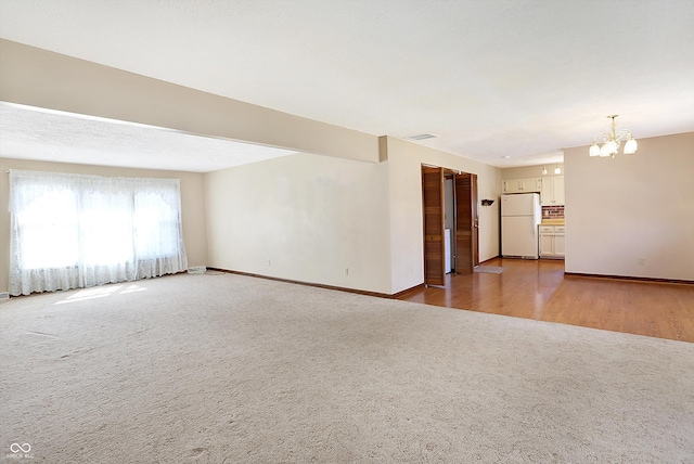 carpeted spare room with visible vents, baseboards, and a notable chandelier