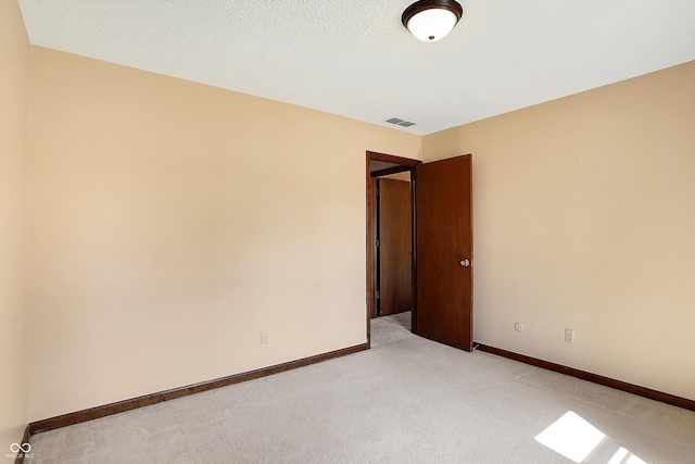 unfurnished room with a textured ceiling, visible vents, baseboards, and light carpet