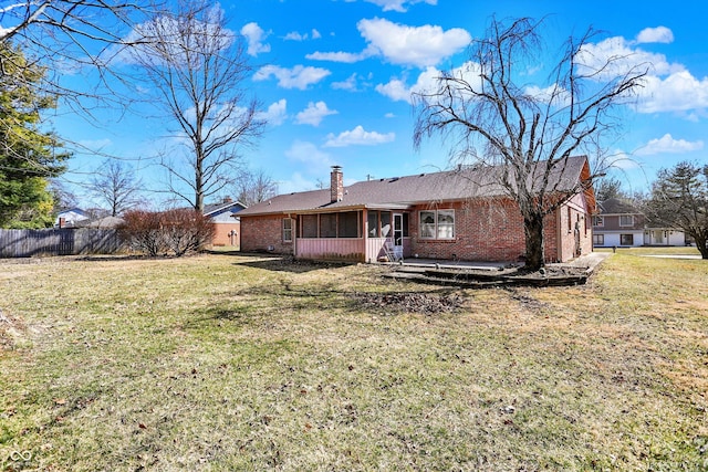 rear view of house with brick siding, fence, a chimney, a yard, and a sunroom