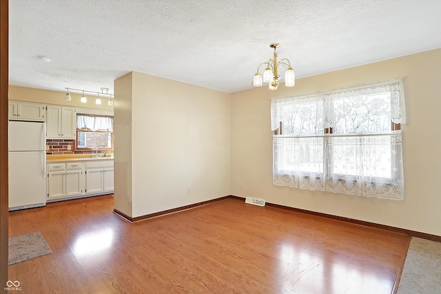 unfurnished dining area with a sink, a textured ceiling, wood finished floors, an inviting chandelier, and baseboards