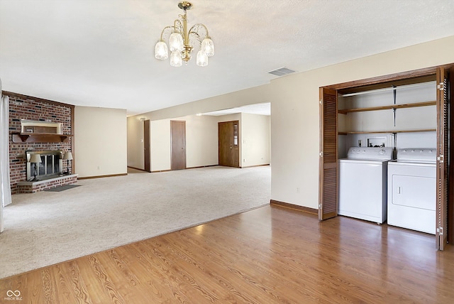 unfurnished living room with visible vents, a notable chandelier, washer and clothes dryer, wood finished floors, and carpet floors