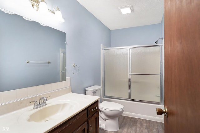 full bathroom featuring toilet, vanity, wood finished floors, combined bath / shower with glass door, and a textured ceiling