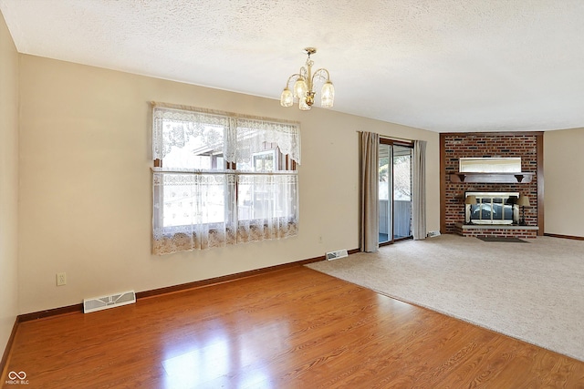 unfurnished living room featuring visible vents, wood finished floors, a textured ceiling, and a chandelier