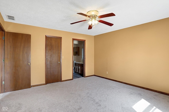 unfurnished bedroom featuring carpet, visible vents, baseboards, ensuite bathroom, and a textured ceiling