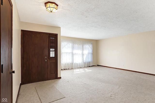 foyer entrance with baseboards, light colored carpet, and a textured ceiling