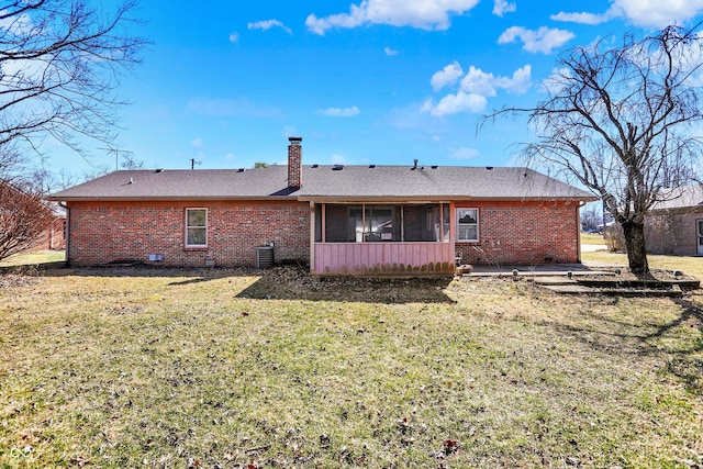 back of house featuring a lawn, brick siding, a sunroom, and a chimney