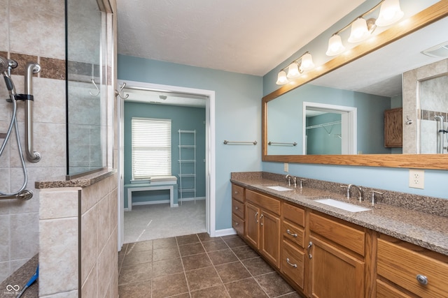 bathroom featuring double vanity, visible vents, a tile shower, and a sink