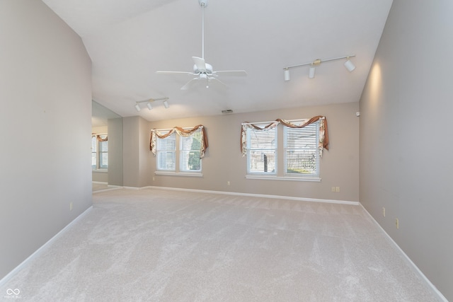 carpeted empty room with lofted ceiling, rail lighting, a ceiling fan, and baseboards