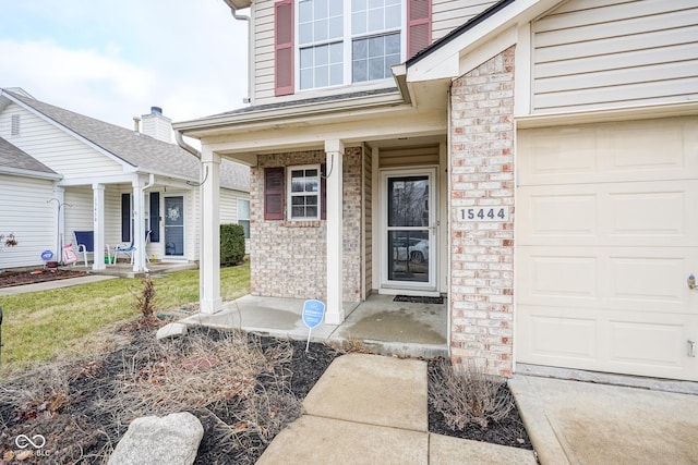 doorway to property with a porch, an attached garage, and brick siding