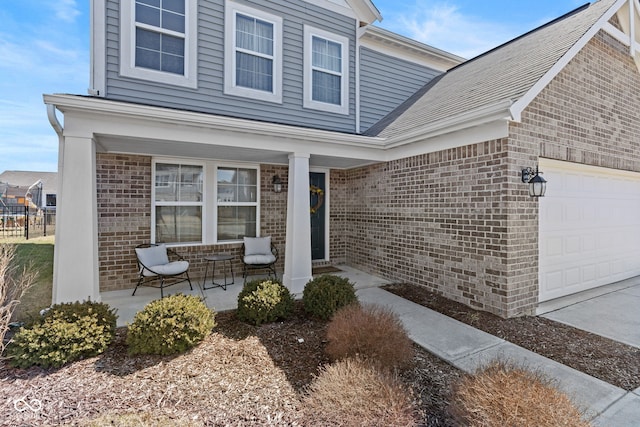 doorway to property featuring a garage, brick siding, and covered porch