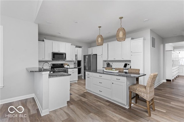 kitchen featuring a kitchen bar, wood finished floors, white cabinetry, and stainless steel appliances