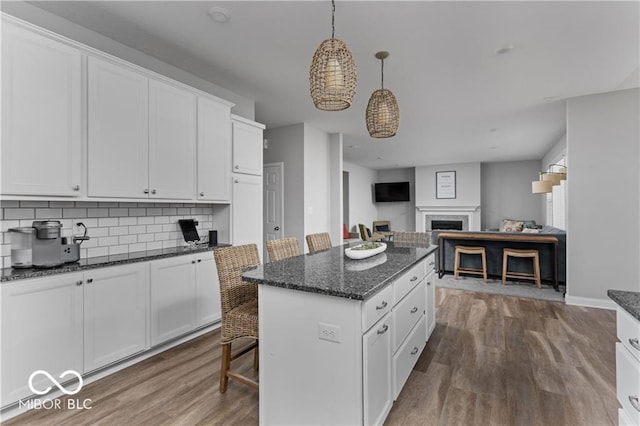 kitchen with tasteful backsplash, a kitchen island, a fireplace, wood finished floors, and white cabinetry