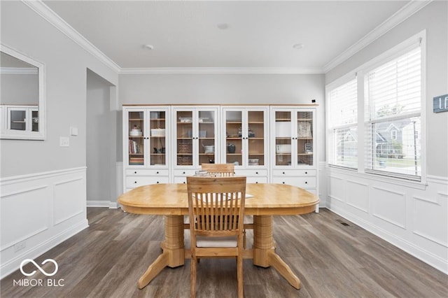 dining room featuring dark wood-style floors, a wainscoted wall, a decorative wall, and crown molding