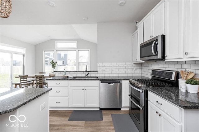 kitchen with dark stone countertops, a peninsula, a sink, white cabinets, and appliances with stainless steel finishes