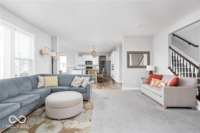 living area featuring stairs, light colored carpet, and baseboards