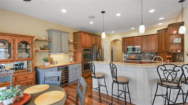 kitchen with beverage cooler, open shelves, arched walkways, a peninsula, and appliances with stainless steel finishes