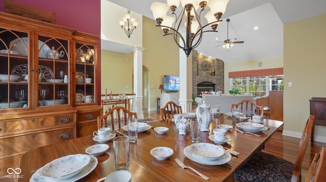 dining area with ceiling fan with notable chandelier, a fireplace, high vaulted ceiling, and ornate columns