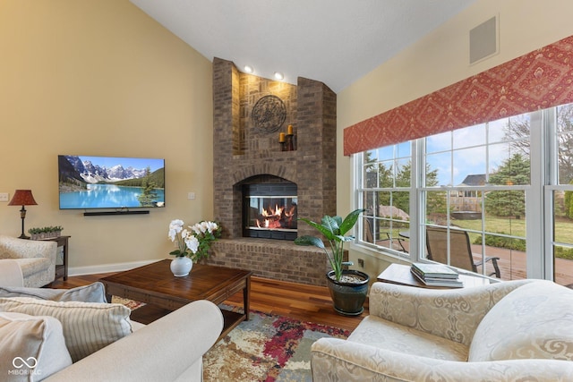 living area featuring visible vents, high vaulted ceiling, wood finished floors, a fireplace, and baseboards