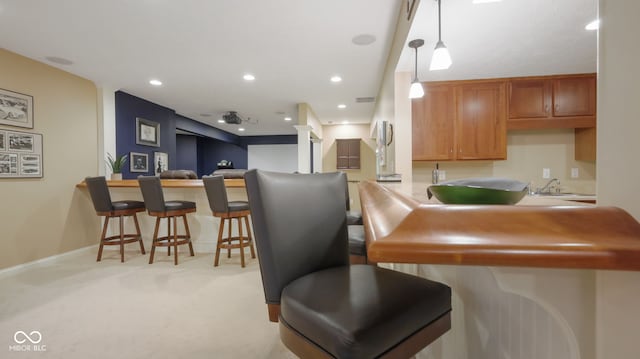 kitchen featuring light colored carpet, a breakfast bar area, recessed lighting, a peninsula, and brown cabinetry