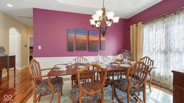 dining area with visible vents, a wainscoted wall, wood finished floors, arched walkways, and a notable chandelier