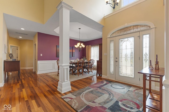 foyer with wood finished floors, a wainscoted wall, ornate columns, visible vents, and an inviting chandelier