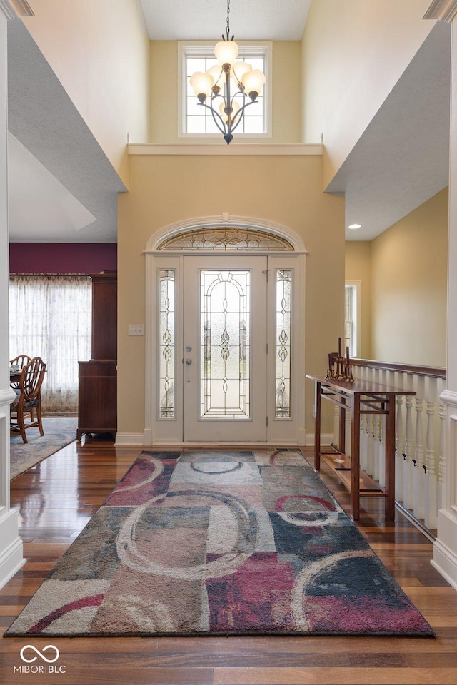 entryway featuring baseboards, a high ceiling, an inviting chandelier, and wood finished floors