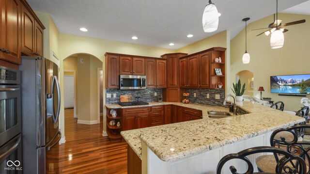 kitchen featuring a sink, open shelves, stainless steel appliances, arched walkways, and a peninsula