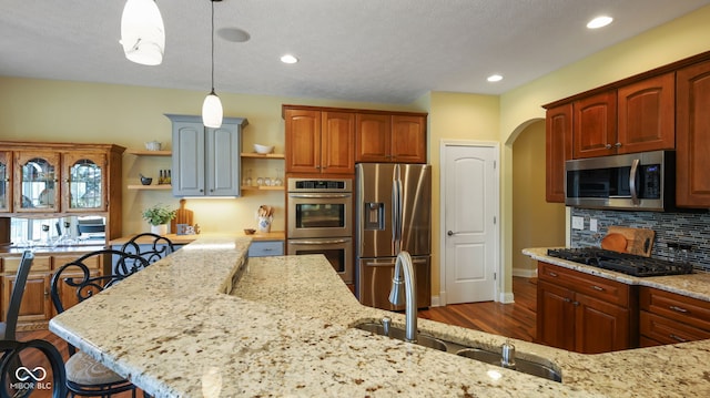 kitchen featuring light stone counters, open shelves, arched walkways, a sink, and stainless steel appliances