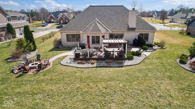 back of house with a lawn, a deck, an outdoor fire pit, brick siding, and a chimney