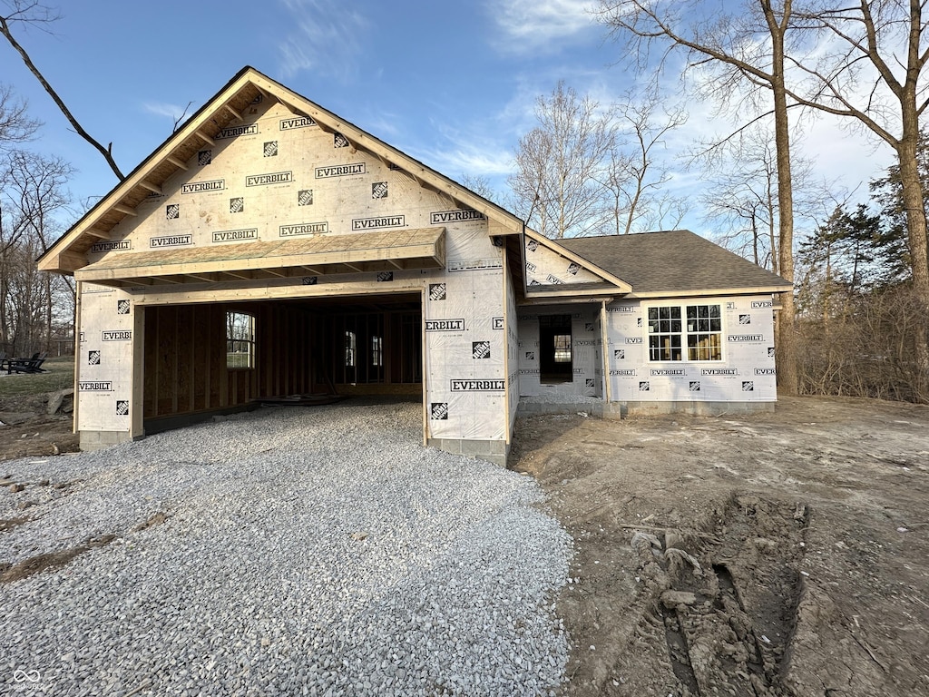 unfinished property with a garage, driveway, and a shingled roof