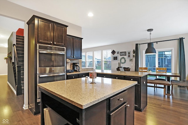 kitchen with dark wood-style floors, dark brown cabinetry, a center island, and light stone counters