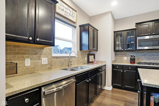 kitchen with light stone counters, light wood finished floors, a sink, glass insert cabinets, and appliances with stainless steel finishes