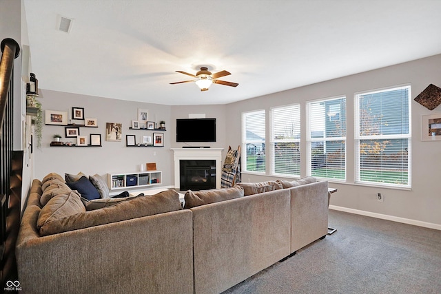 carpeted living area featuring visible vents, baseboards, a glass covered fireplace, and a ceiling fan