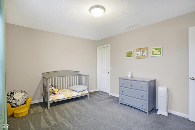 carpeted bedroom with a nursery area, a textured ceiling, and baseboards