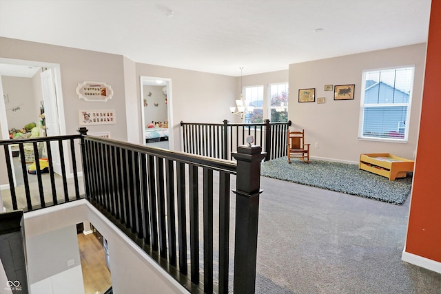 corridor featuring an inviting chandelier, an upstairs landing, baseboards, and carpet floors