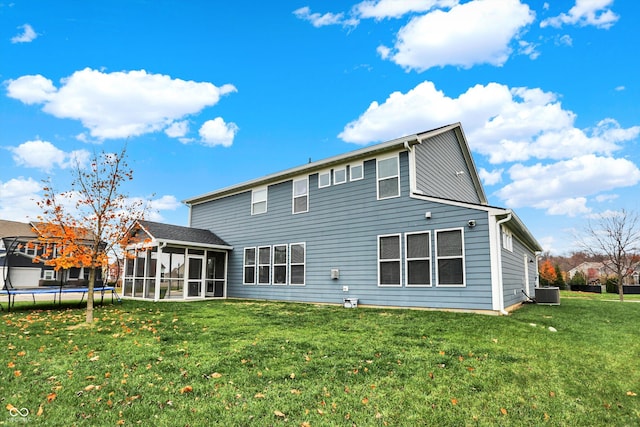 rear view of house featuring central air condition unit, a trampoline, a lawn, and a sunroom