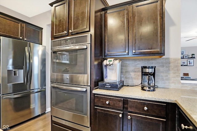 kitchen with light wood-type flooring, appliances with stainless steel finishes, decorative backsplash, light stone countertops, and dark brown cabinets