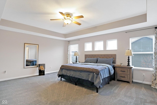 carpeted bedroom with a tray ceiling, a ceiling fan, and baseboards