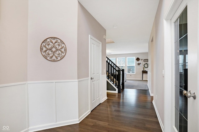 hall featuring dark wood-type flooring, stairway, a decorative wall, and a wainscoted wall