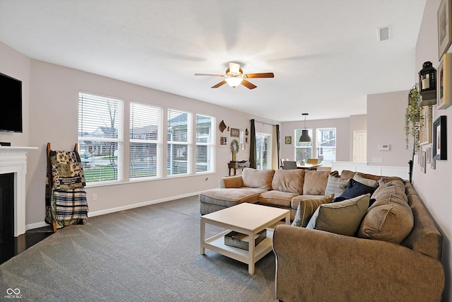 living room featuring visible vents, baseboards, a fireplace with flush hearth, a ceiling fan, and dark colored carpet