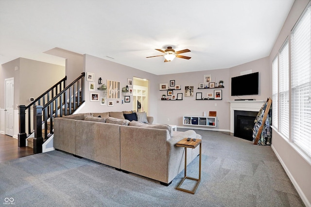 carpeted living room with stairs, a fireplace with flush hearth, baseboards, and ceiling fan