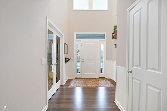 entryway featuring a towering ceiling, a healthy amount of sunlight, dark wood-style flooring, and french doors