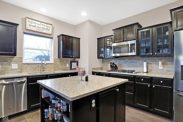 kitchen with light wood finished floors, a kitchen island, a sink, stainless steel appliances, and glass insert cabinets