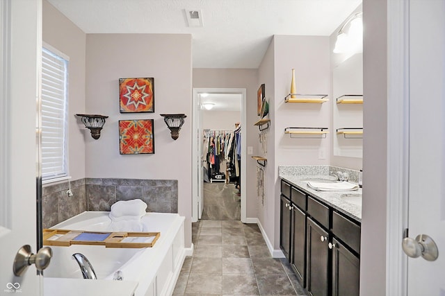 full bathroom featuring a spacious closet, visible vents, tile patterned flooring, a garden tub, and vanity