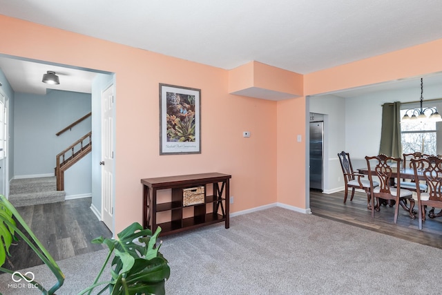 sitting room featuring wood finished floors, carpet, baseboards, stairs, and a chandelier