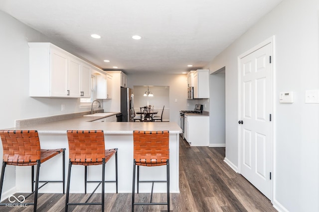 kitchen featuring a sink, a peninsula, white cabinets, stainless steel appliances, and dark wood-style flooring