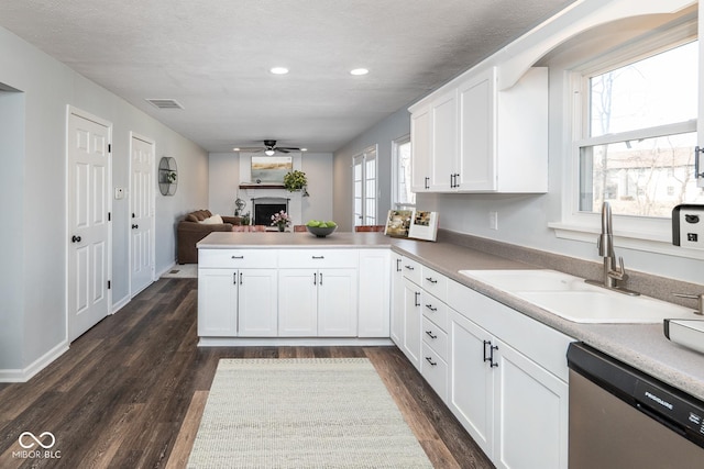 kitchen featuring visible vents, a peninsula, a fireplace, a sink, and stainless steel dishwasher