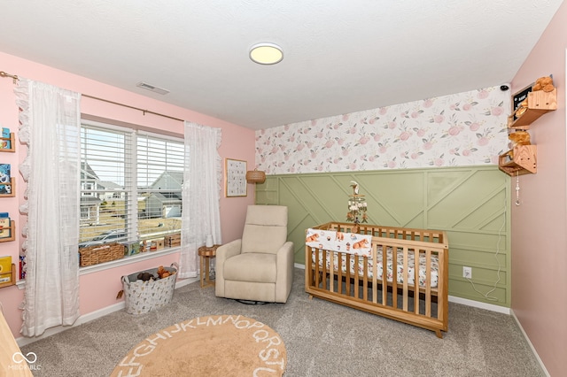 bedroom with visible vents, baseboards, wallpapered walls, a crib, and carpet flooring