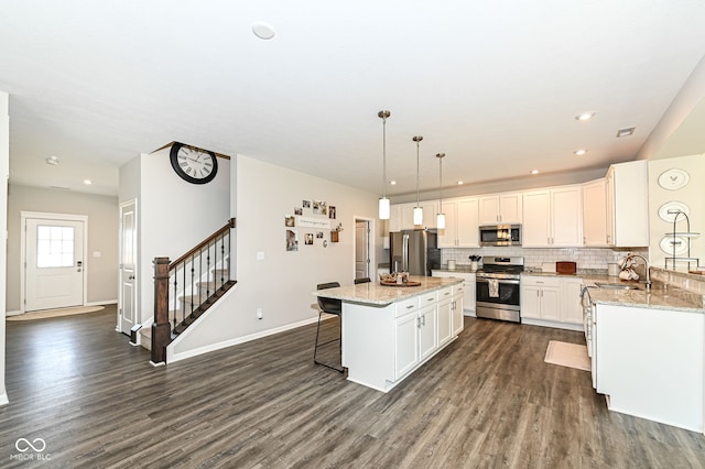 kitchen featuring dark wood finished floors, a sink, appliances with stainless steel finishes, backsplash, and a center island