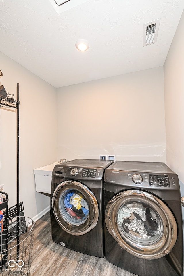 clothes washing area featuring wood finished floors, visible vents, washing machine and clothes dryer, laundry area, and a sink